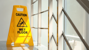 Yellow caution wet floor sign placed near large office windows to prevent slip-and-fall incidents.