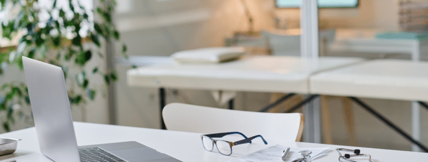 Doctor’s office desk with laptop, stethoscope, and paperwork