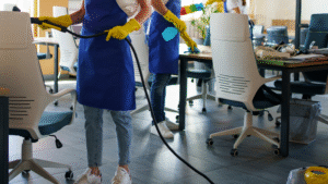Professional cleaners in blue aprons disinfecting and steam-cleaning an office workspace.