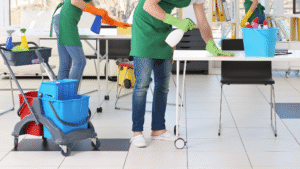 Commercial cleaning crew using disinfectants and carts to clean office tables and surfaces.