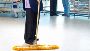 Custodian mopping floor in a medical facility with a dust mop
