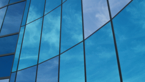 Modern glass building exterior reflecting blue sky and clouds.