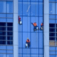Professional cleaner suspended on ropes washing windows of a high-rise building.