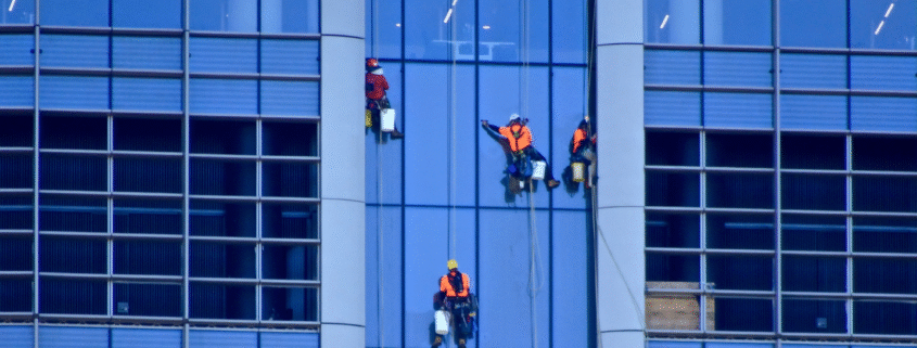 Professional cleaner suspended on ropes washing windows of a high-rise building.