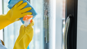 Gloved hands spraying and wiping down a window with cleaning solution