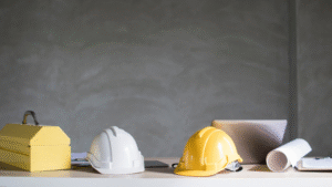 White and yellow construction helmets placed on a clean desk next to blueprints and tools.