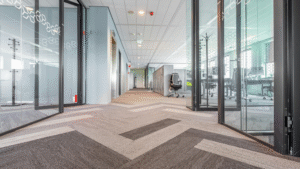 Long modern office hallway with patterned carpet and glass partitions.