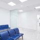 Bright hospital waiting room with blue chairs lined against the wall.