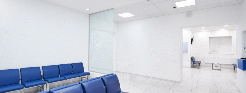 Bright hospital waiting room with blue chairs lined against the wall.