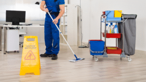 Worker mopping an office floor with a wet floor sign placed nearby.