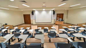 Empty lecture hall with desks and a projection screen.