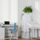 Bright medical exam room with clean desk, blue chair, white coat hanging, and exam table prepared for patients.