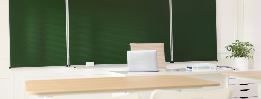 Clean and organized classroom with green board and teacher desk prepared for students