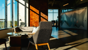 Modern office lounge area with seating, glass table, and large windows in a clean corporate workspace