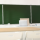 Teacher desk with laptop in clean classroom with chalkboard