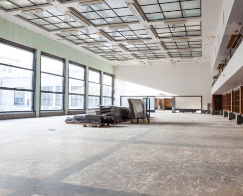 Empty commercial interior with large windows and unfinished floors ready for cleaning