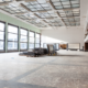 Empty commercial interior with large windows and unfinished floors ready for cleaning