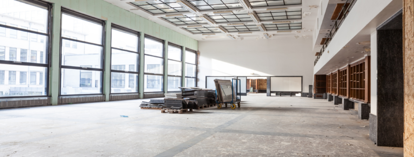 Empty commercial interior with large windows and unfinished floors ready for cleaning