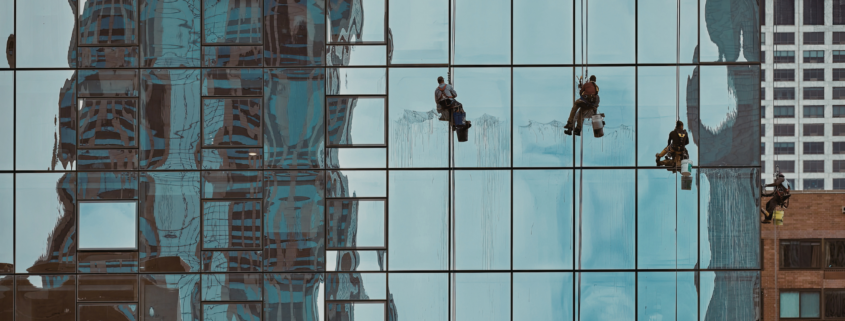 Commercial window cleaners working on large glass facade with reflections