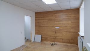 Commercial room during final construction phase with flooring materials, wall panels, and renovation debris still present.