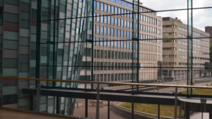 Interior view through large commercial windows overlooking nearby office buildings.